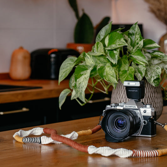 Eine Kamera mit Boho Kameragurt auf einer Kücheninsel mit Pflanzen